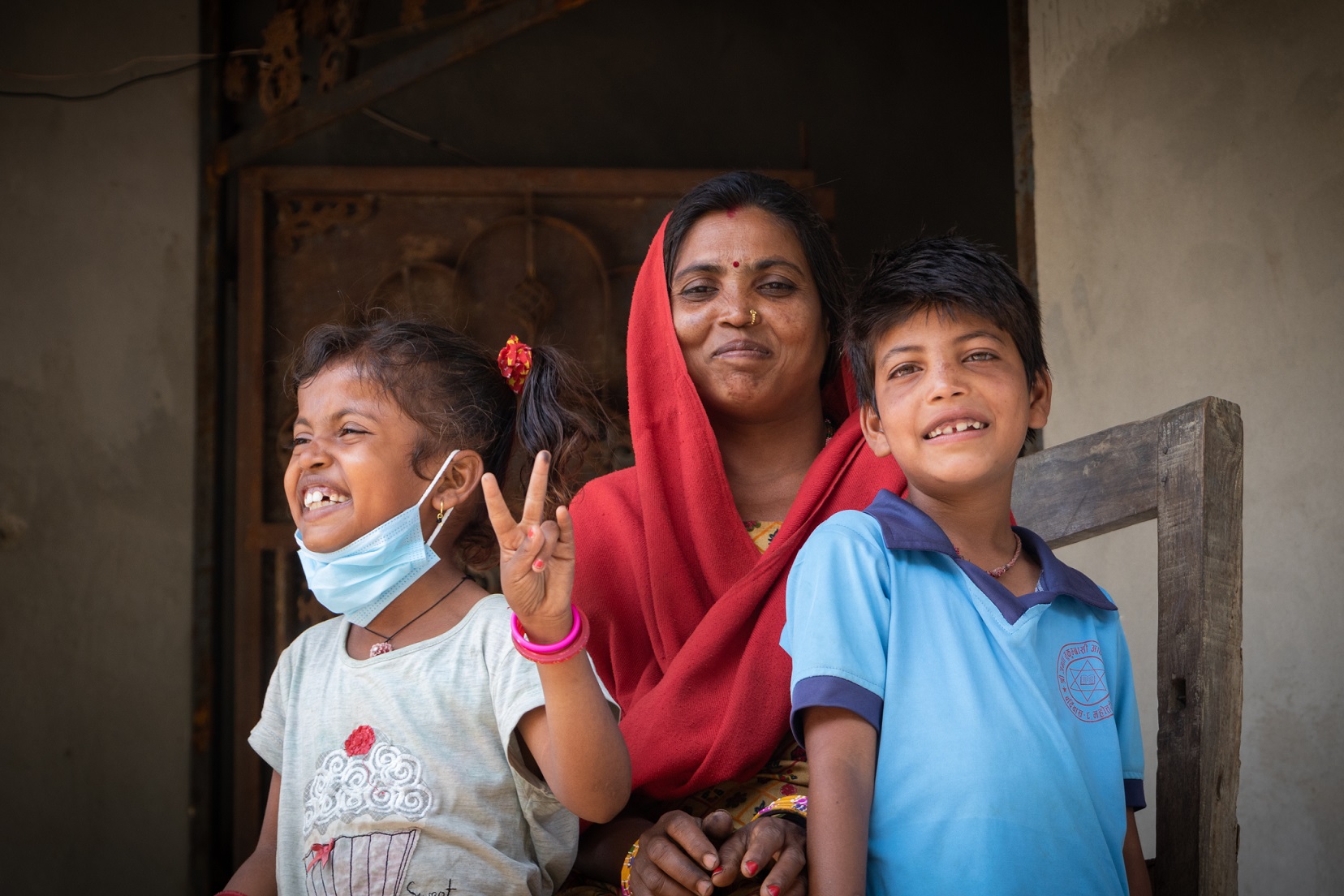 Punaiseen huiviin pukeutunut nepalilainen äiti ja kaksi lastaan poseeraavat kameralle.